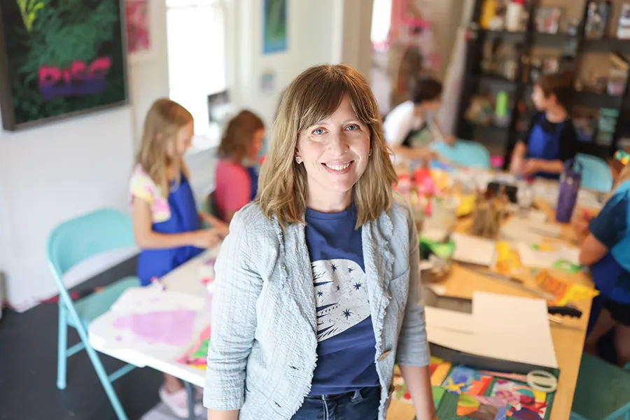 Cara Sullivan standing in the foreground with a group of students in the background working around the studio tables.